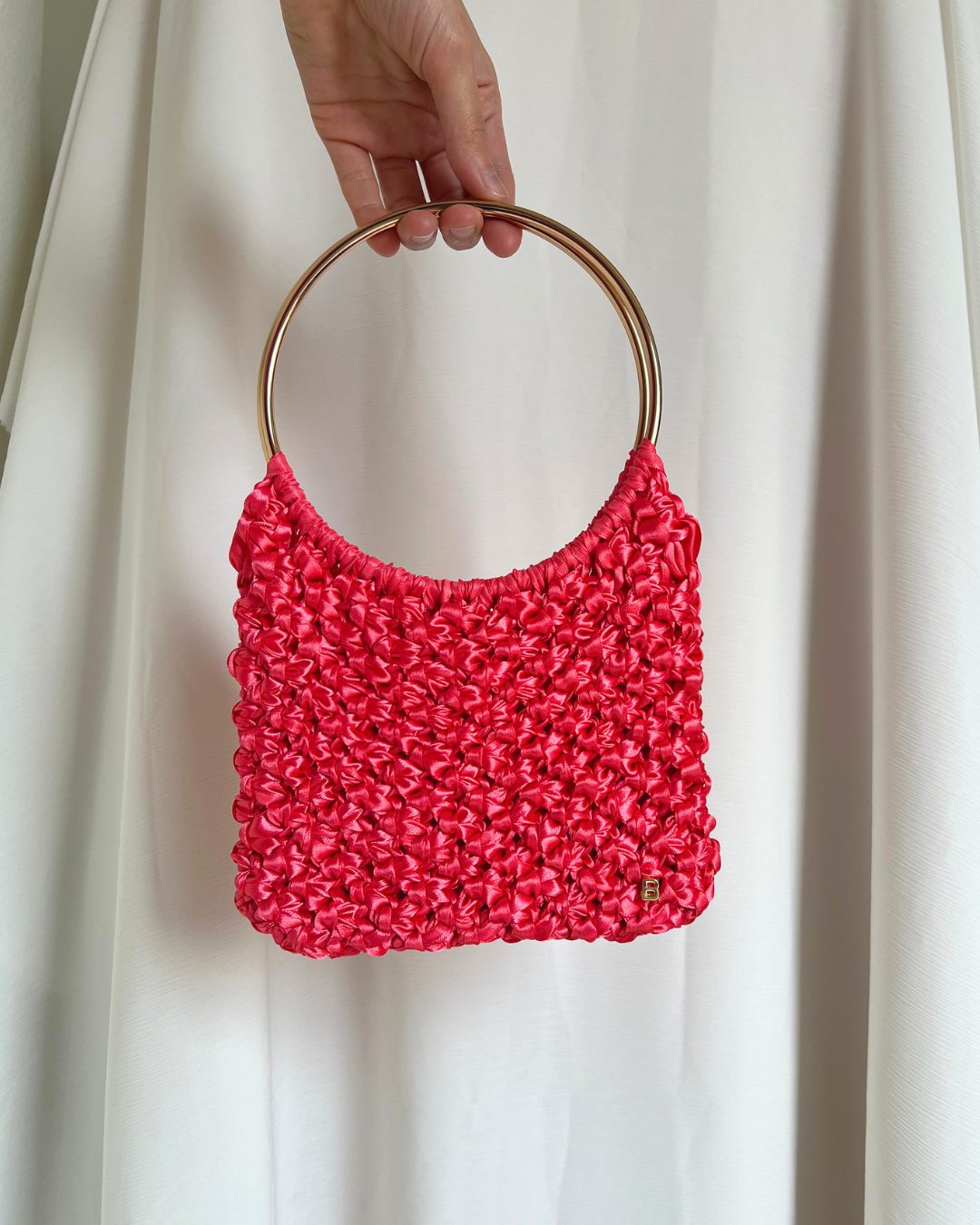Roma Bag de raso coral con asas doradas brillantes, vista frontal, con la B de Bimbú en la esquina inferior derecha.