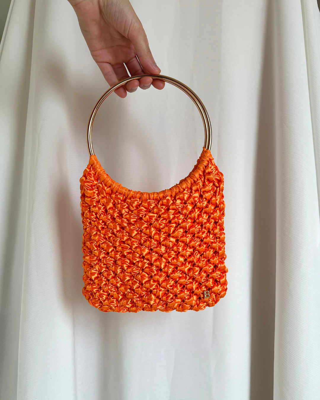 Roma Bag de raso naranja con asas doradas brillantes, vista frontal, con la B de Bimbú en la esquina inferior derecha.